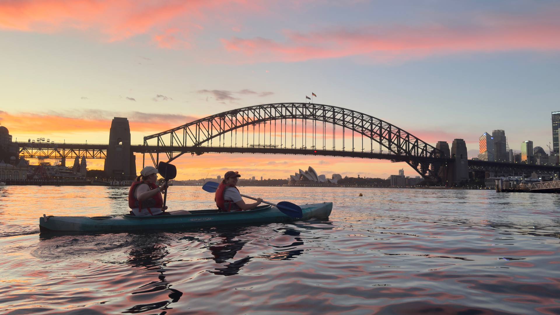 Couple on Sydney Harbour sunset kayak tour under pink sky