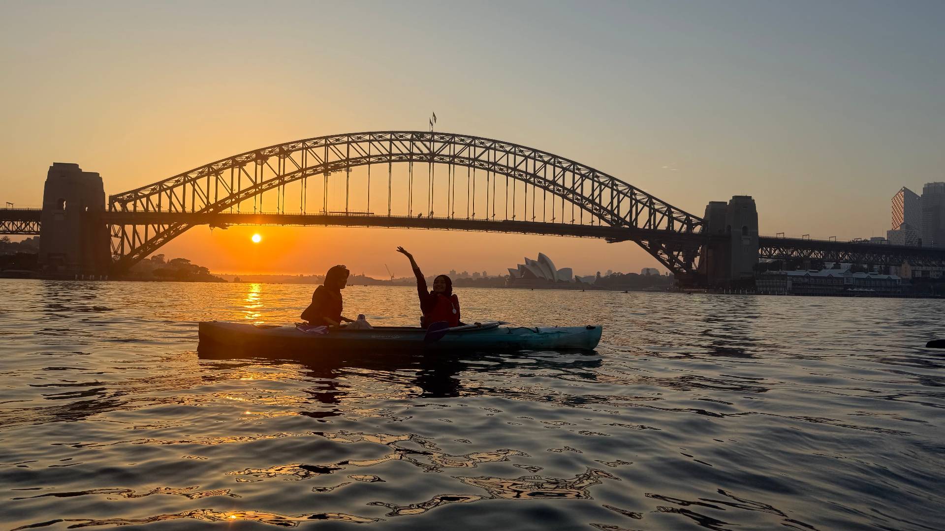 Couple on Sydney Harbour sunset kayak tour waving from kayak