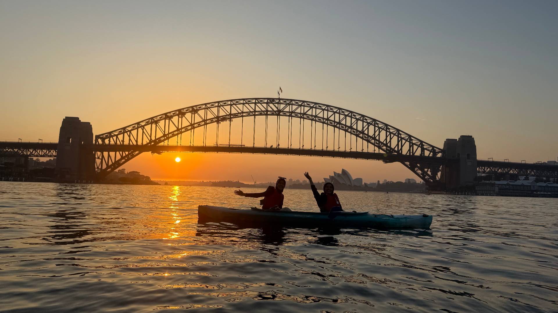 Sydney Kayak Tours – couple waving at golden hour on harbour